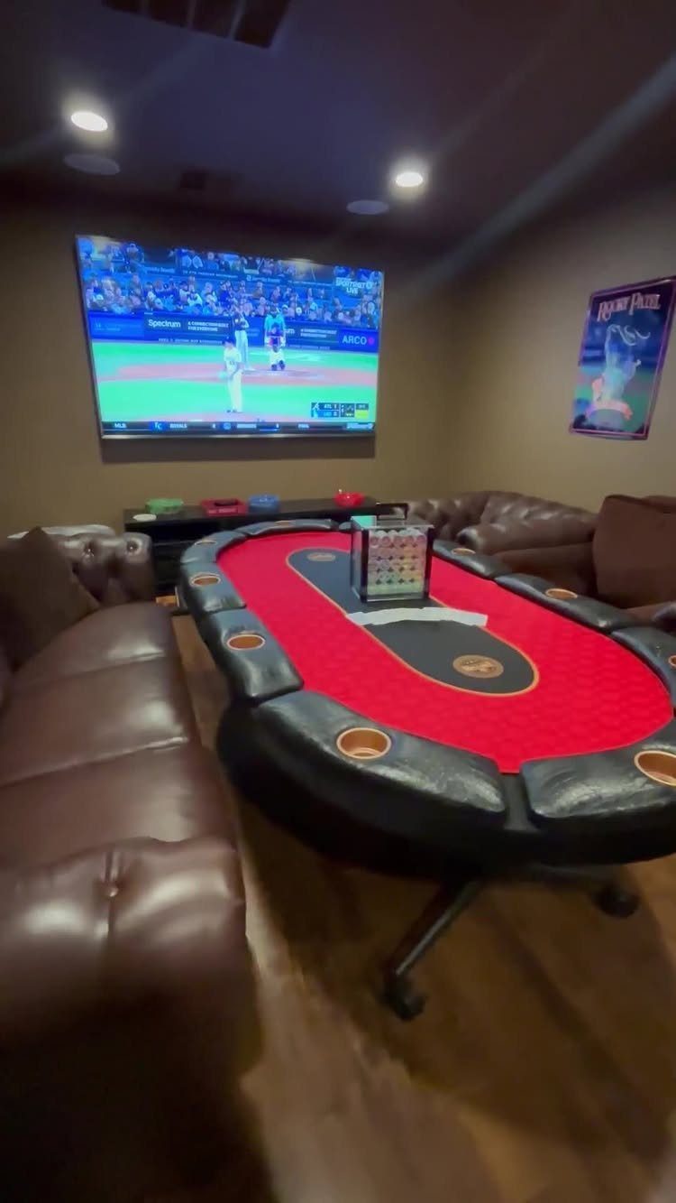 Oval poker table with red felt surrounded by brown leather sofas in game room