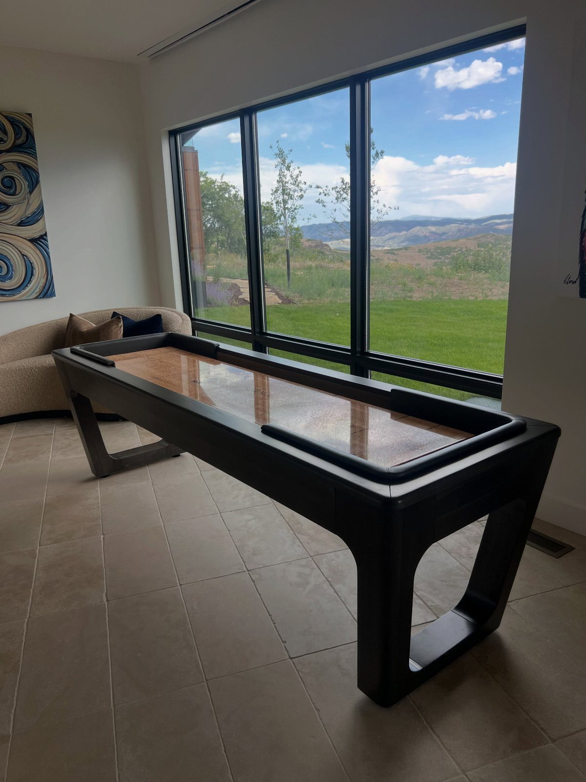 Black shuffleboard table in a bright room with a large window view