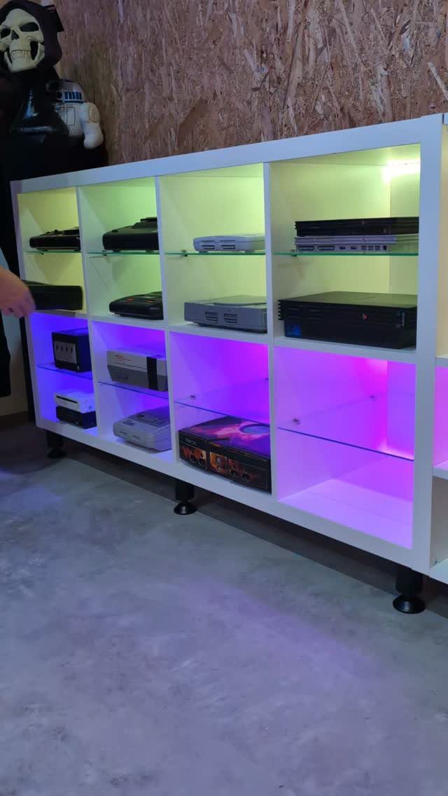 White shelving unit with colorful LED lighting displaying various vintage game consoles