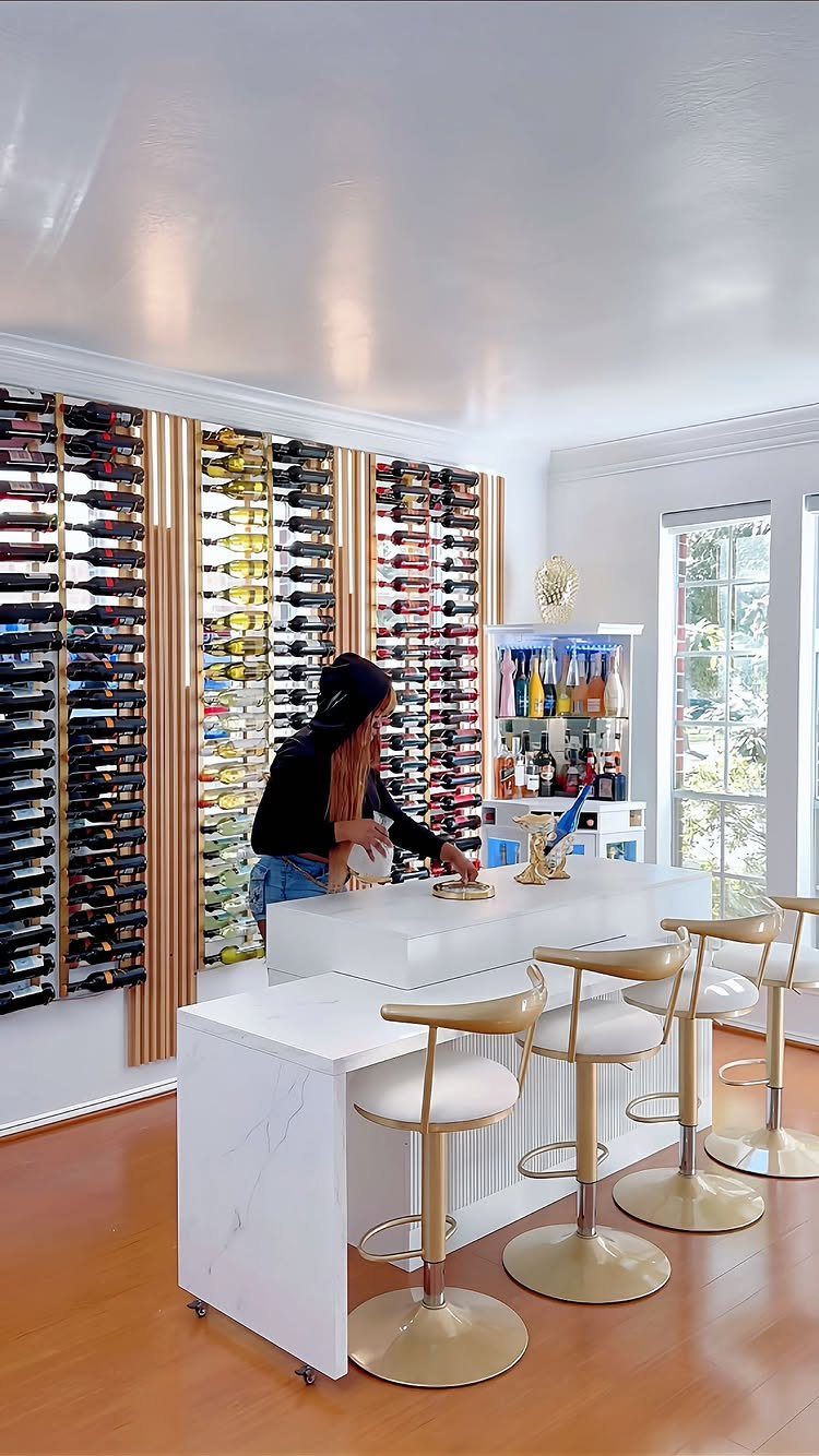 Woman behind a white marble bar with gold bar stools and wine walls.