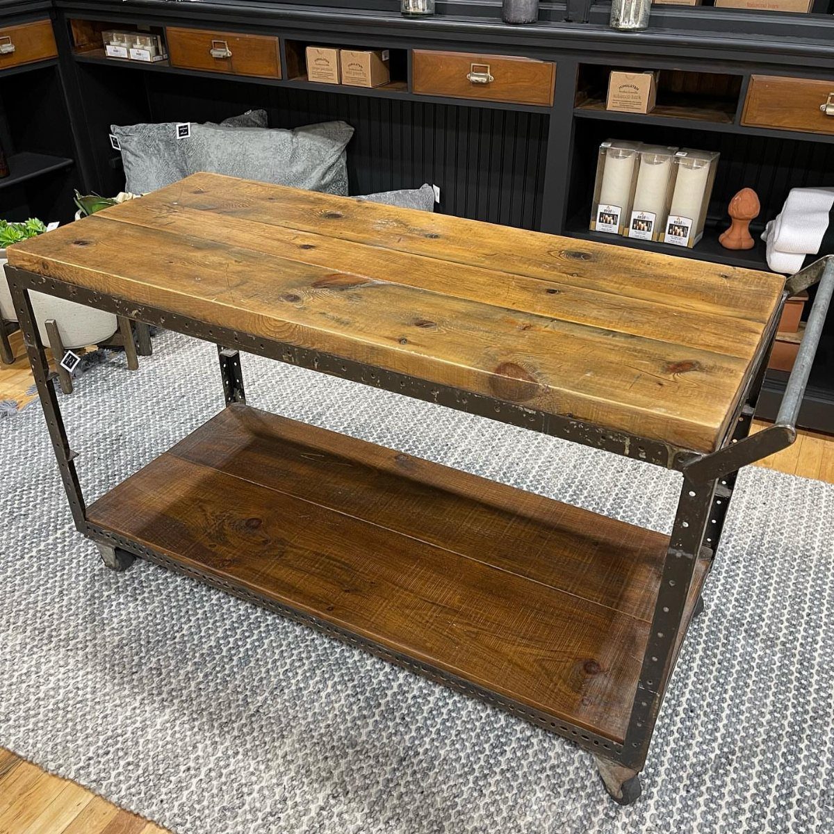 Rustic wooden rolling bar cart with metal frame on a grey patterned rug.