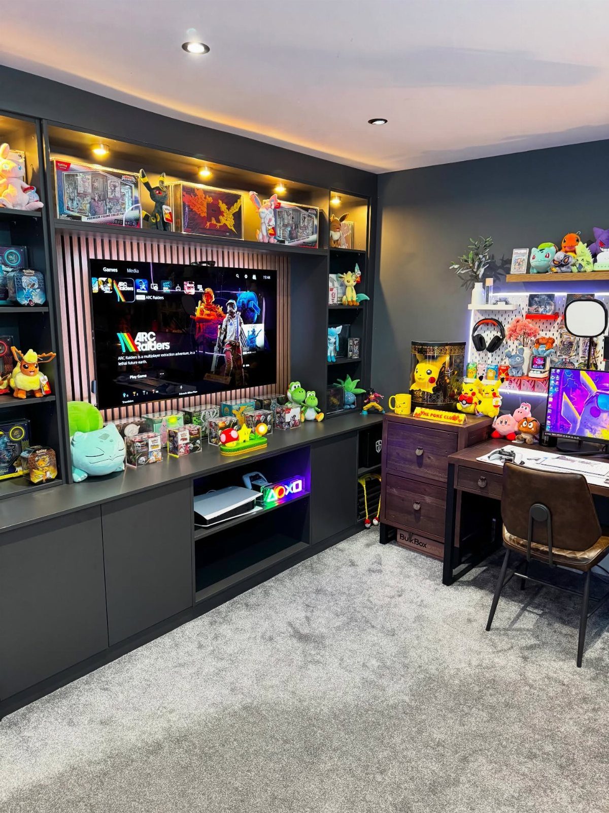 Gaming room with a large TV, collectible figures, and a computer desk setup.