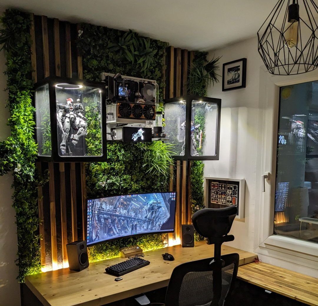 Gaming desk setup with a curved monitor and a wall of green plants.