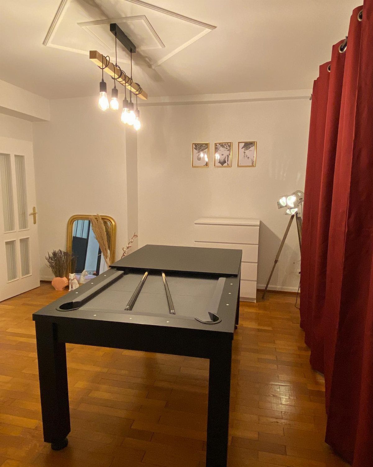 Black shuffleboard table in a modern room with wooden floors and red curtains.