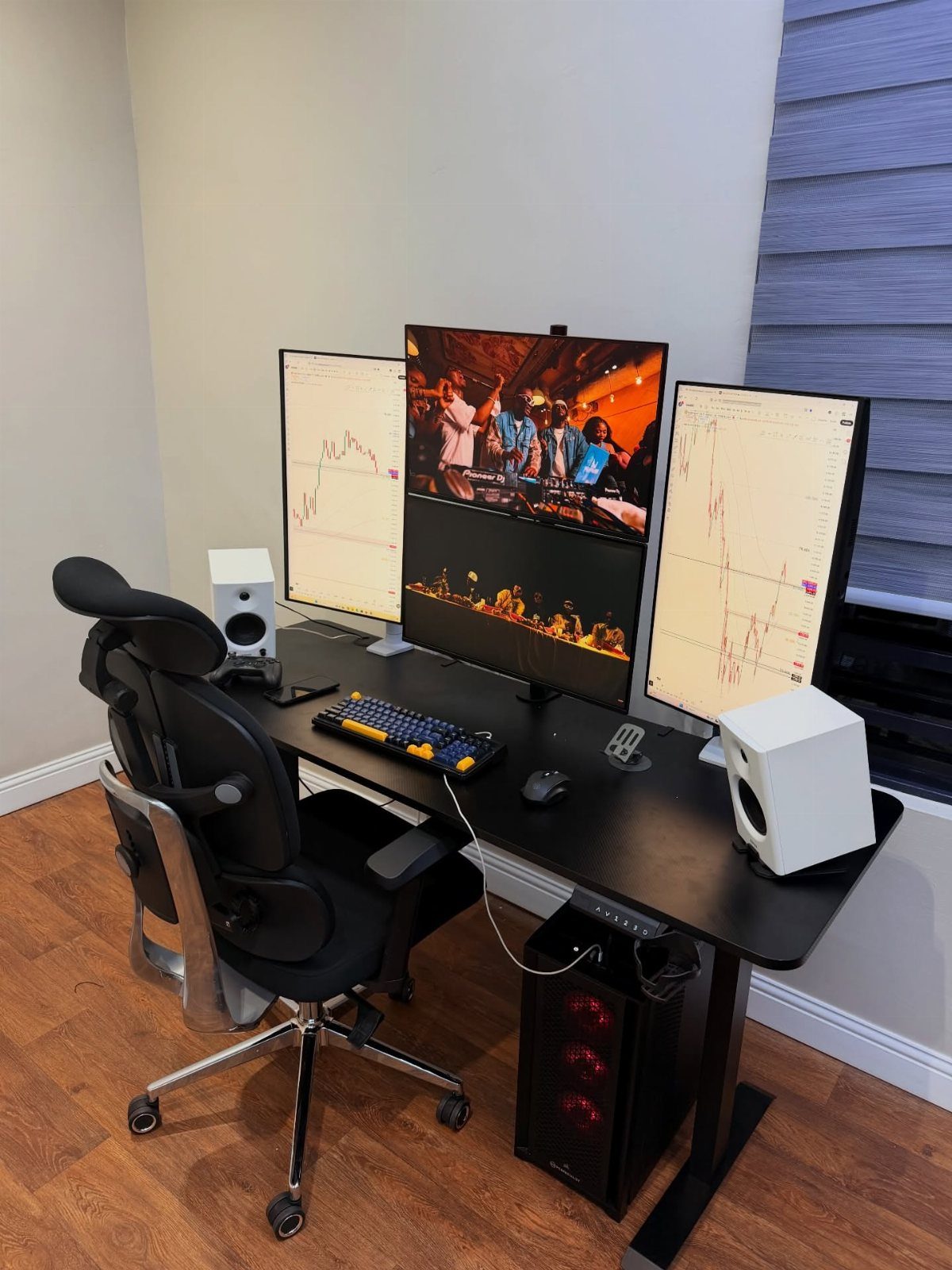 Gaming desk setup with three monitors, ergonomic chair, and PC tower in office.