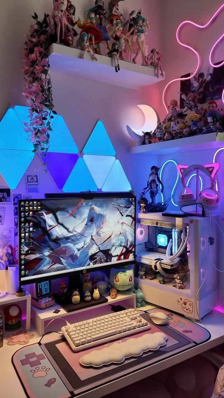 Gaming desk setup with white peripherals, anime figurines, and pink neon wall lighting.