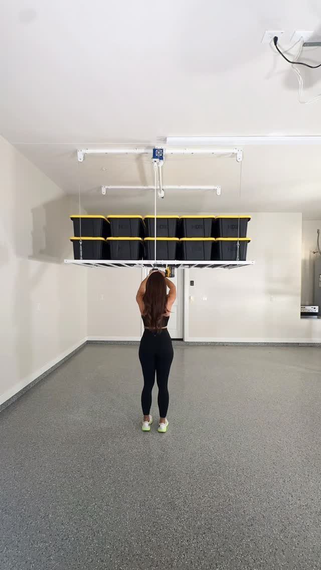 Woman lowering a ceiling storage rack filled with black and yellow bins in garage