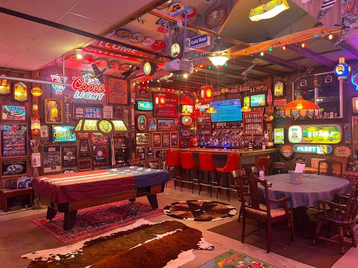 Game room with a pool table and a bar with red stools and neon signs.