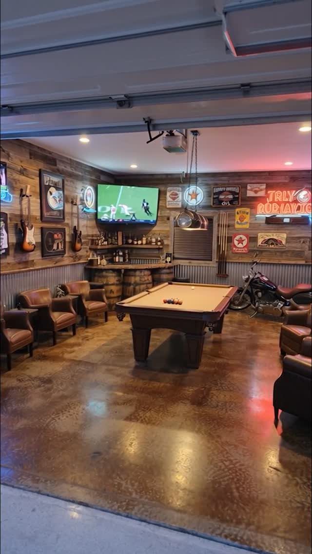 Brown pool table in a rustic garage game room with leather chairs and bar.