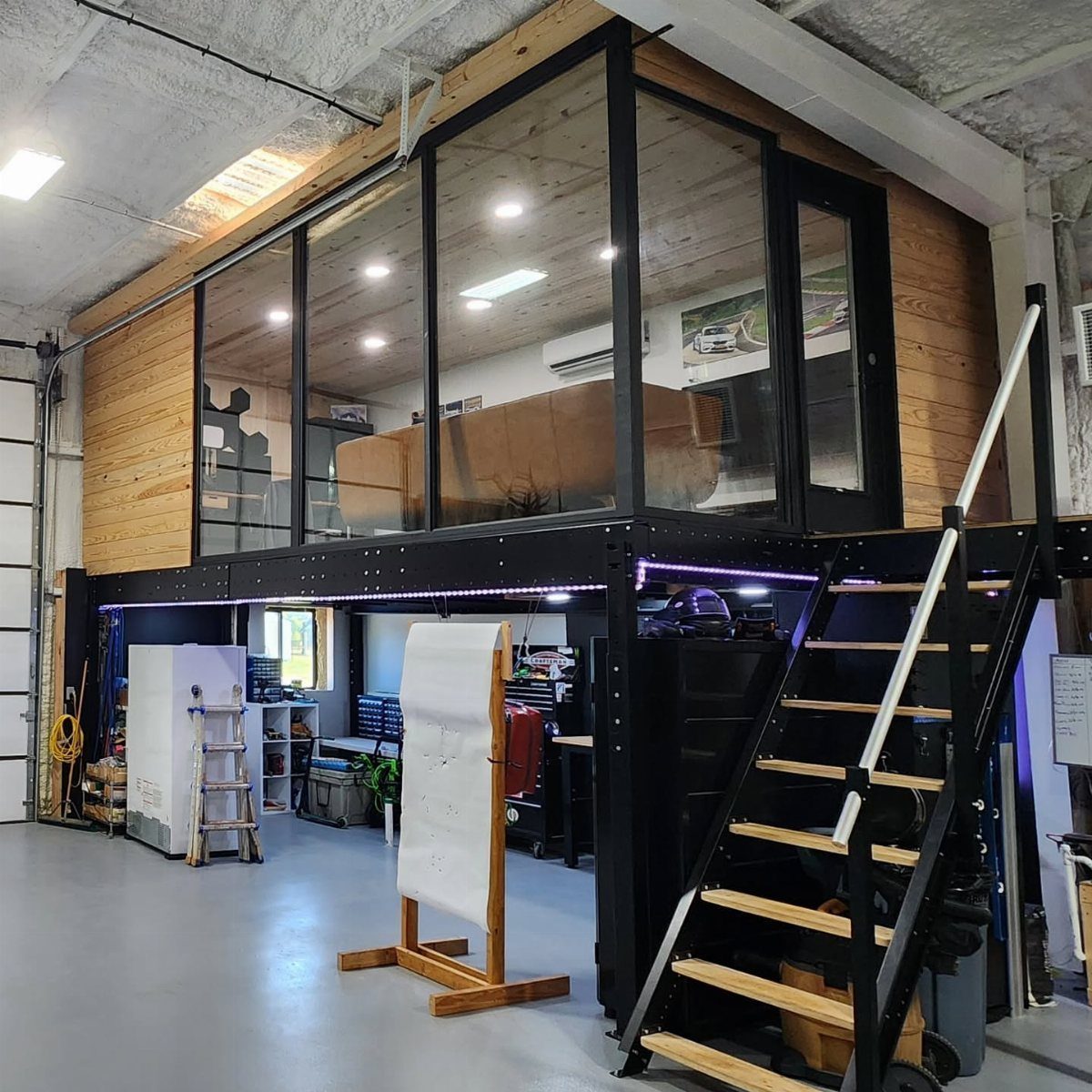 Modern garage loft with glass walls, wooden accents, and a black metal staircase.