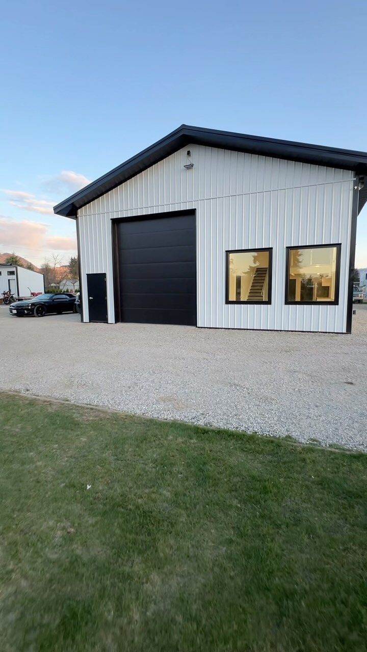 White pole barn garage with black trim and a visible interior loft area.