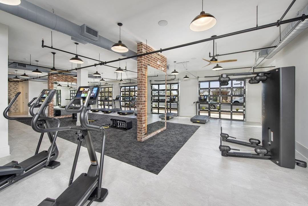 Modern home gym with elliptical machines, treadmills, and industrial lighting in a garage.