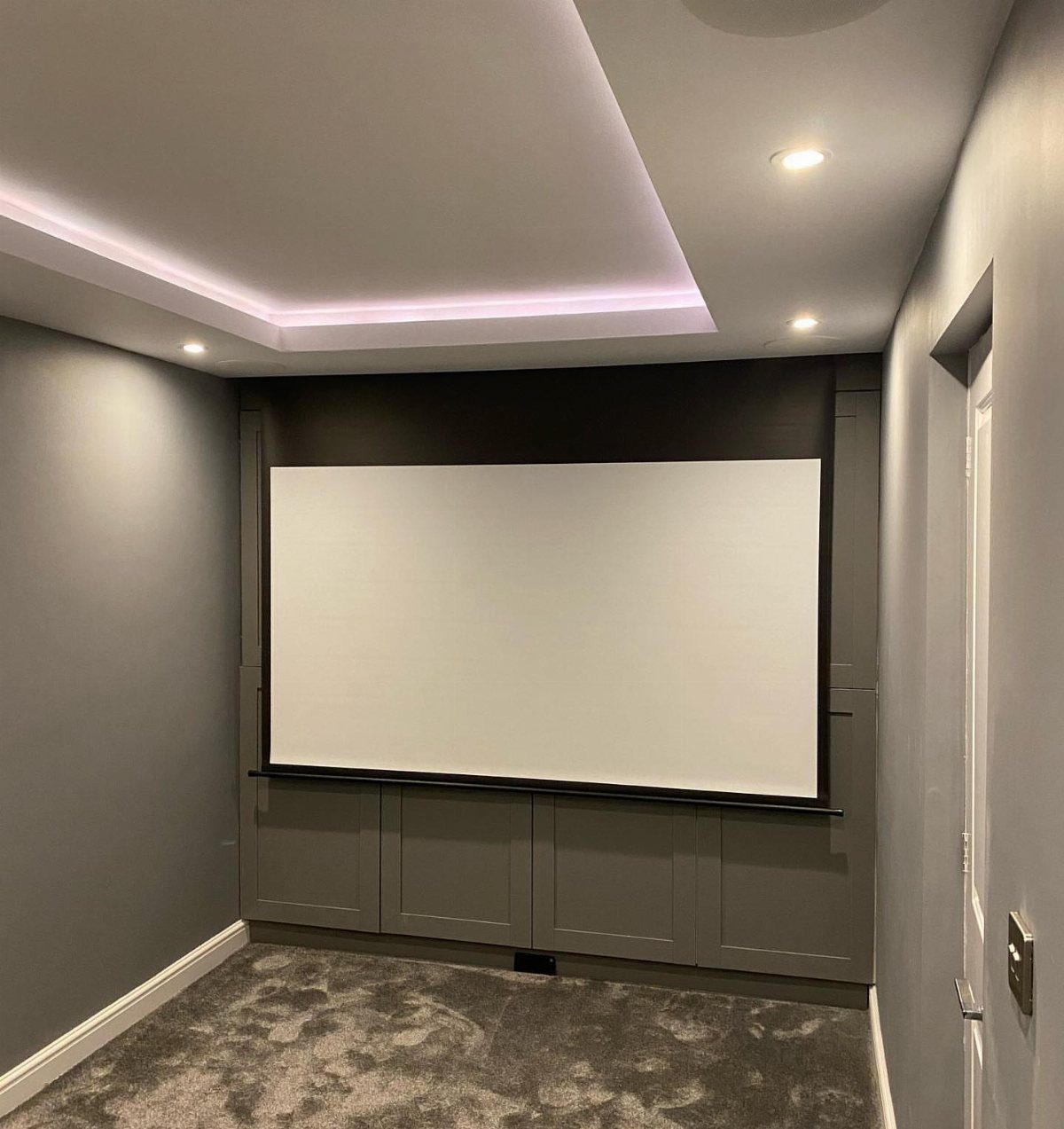 Large white projection screen in a grey room with recessed ceiling lighting.