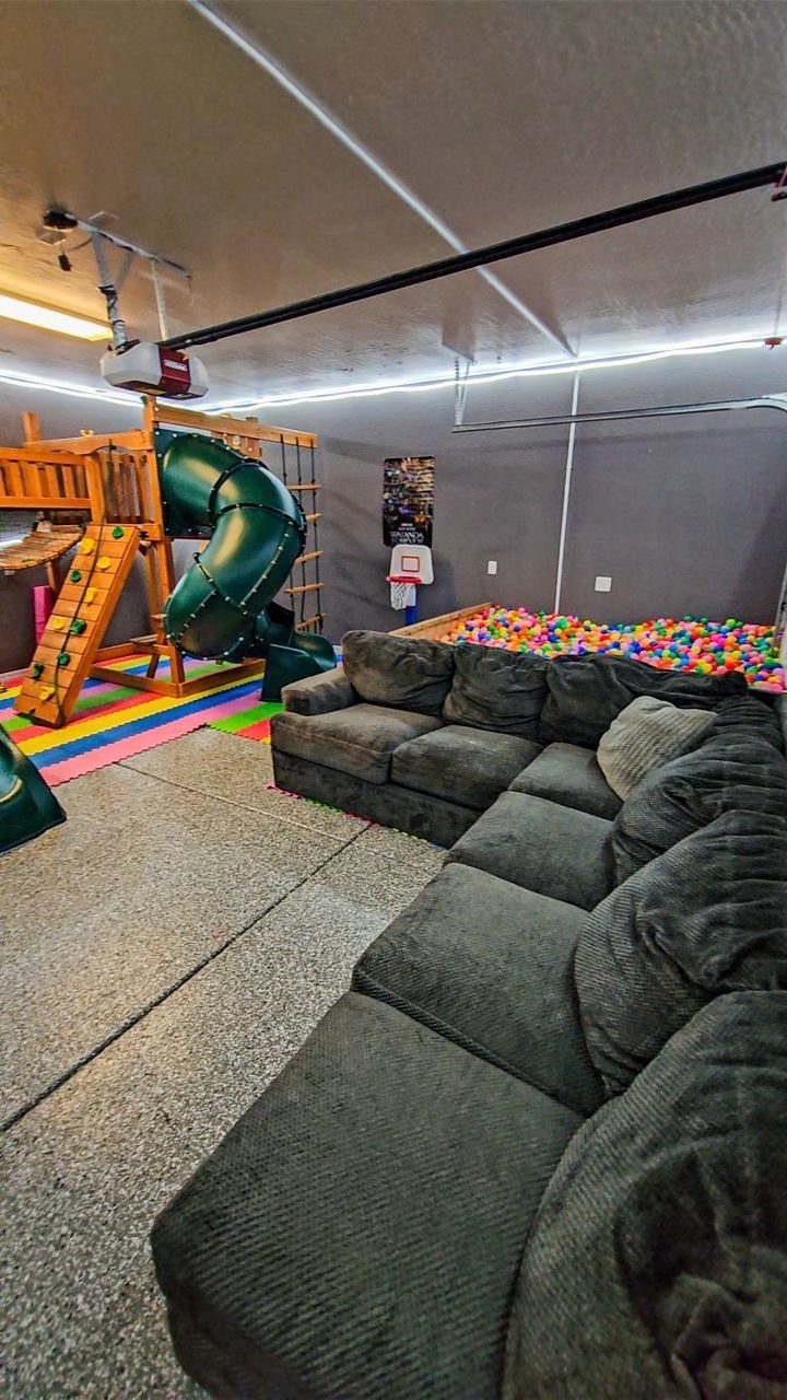 Garage playroom with a large sectional sofa, wooden slide, and colorful ball pit.