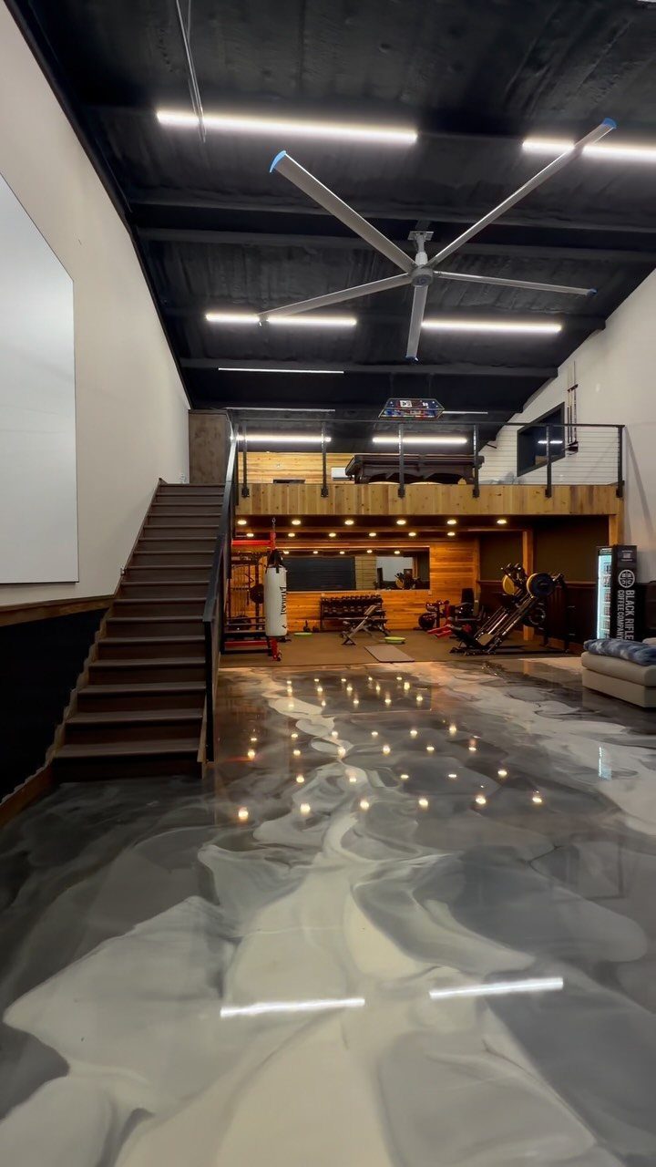 Multi-level garage rec room with metallic floors, gym equipment, and a wooden loft.