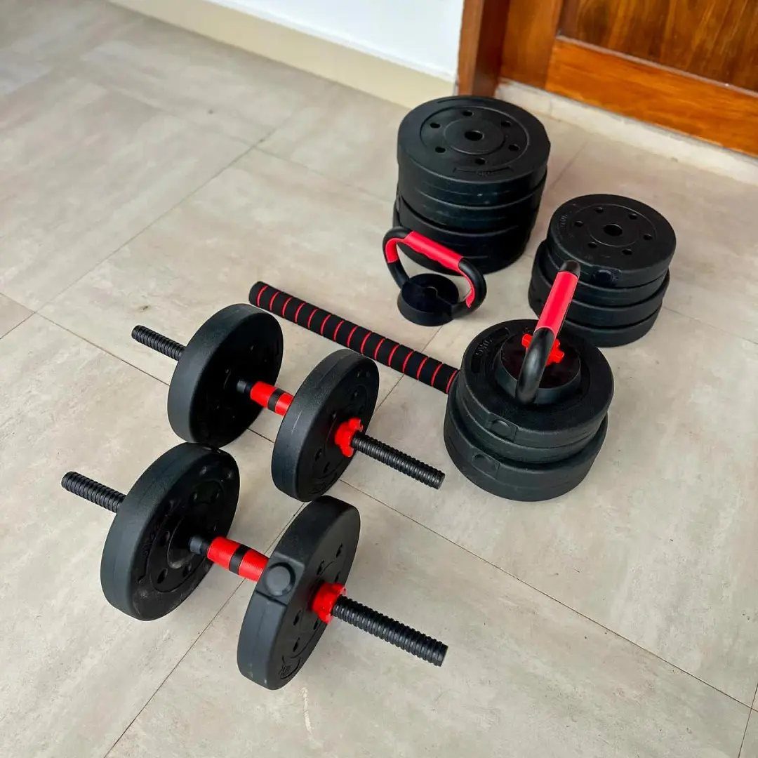 Adjustable dumbbells and black weight plates with red accents on a tiled floor.