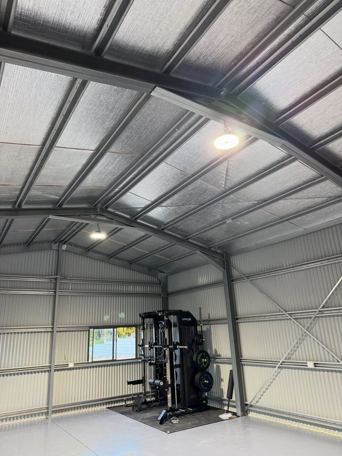 Black multi-gym weight machine inside a corrugated metal garage with insulated ceilings.