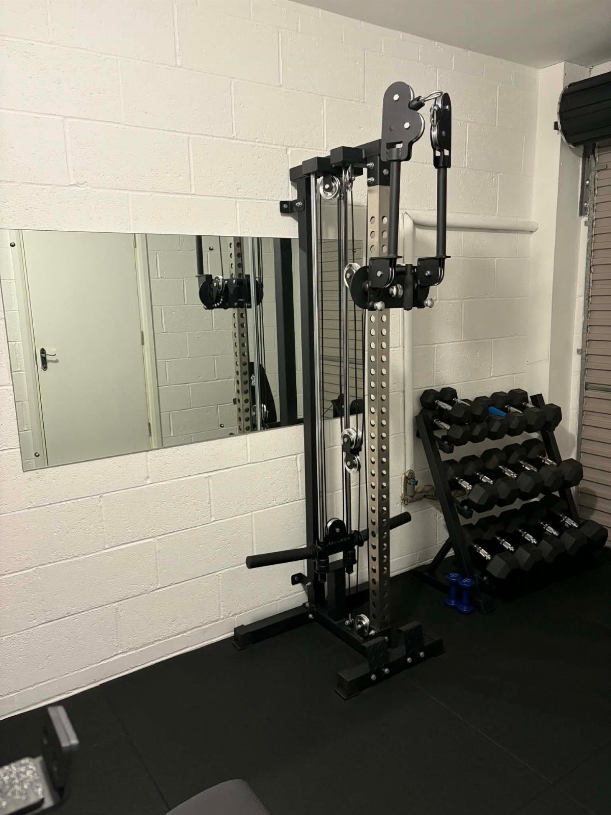 Cable machine and dumbbell rack in a garage gym with white brick walls.