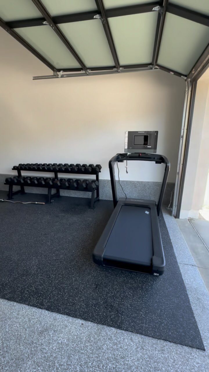 Treadmill and dumbbell rack on a rubber mat in a garage gym
