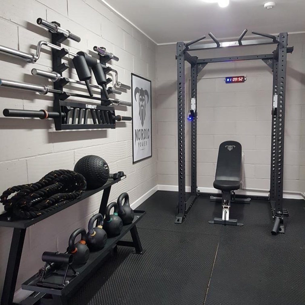 Home gym setup with power rack, kettlebells, and wall-mounted barbells on rubber flooring.
