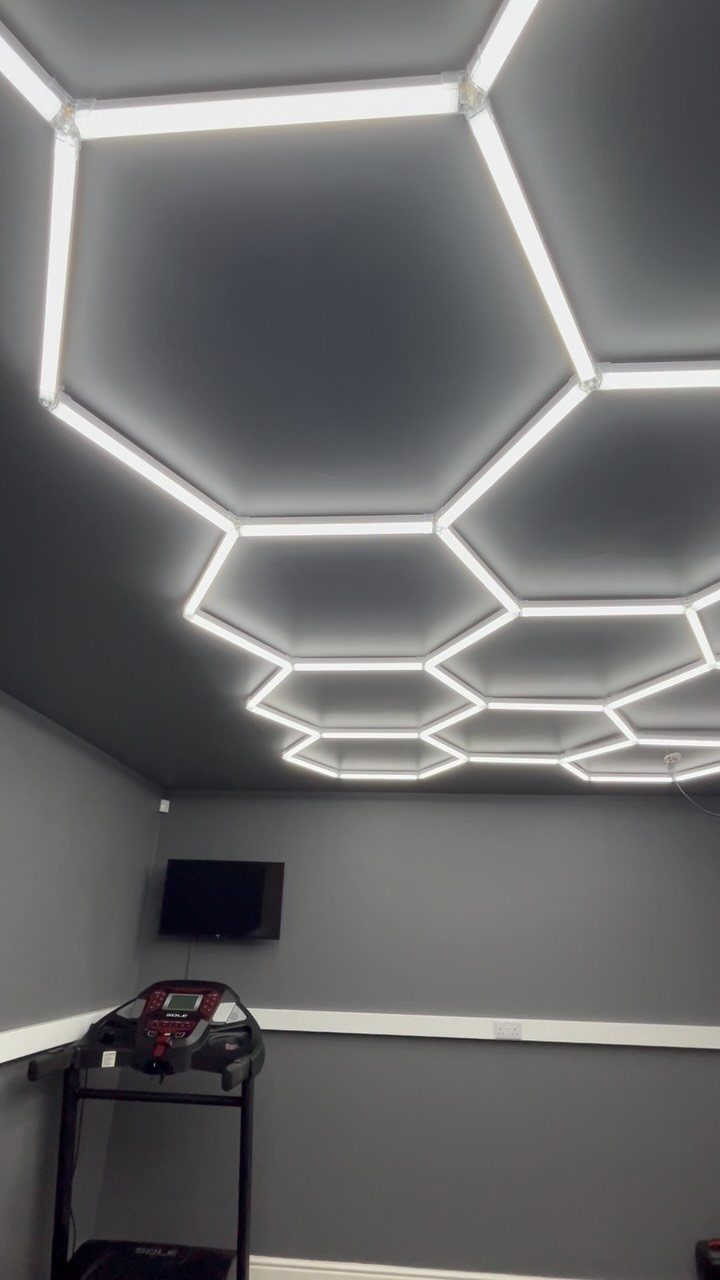 Hexagonal white LED ceiling lights in a grey home gym with a treadmill.