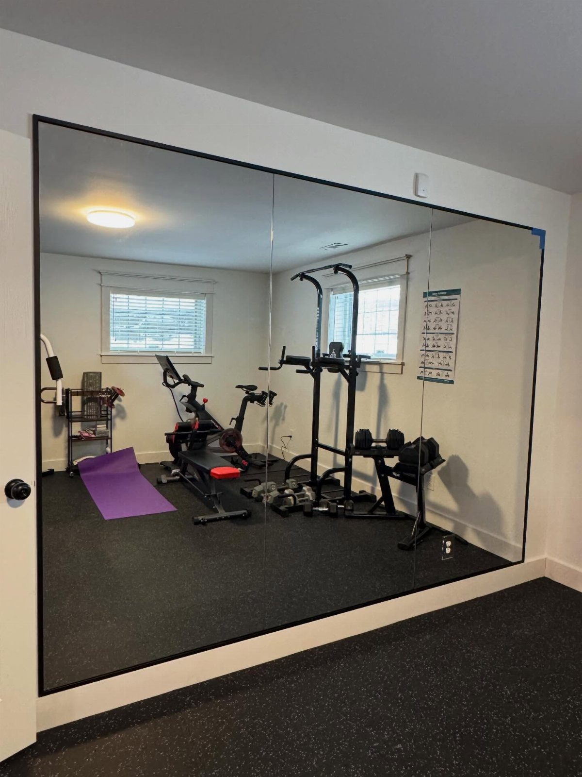 Large wall mirrors in a home gym reflecting weightlifting equipment and rubber flooring.