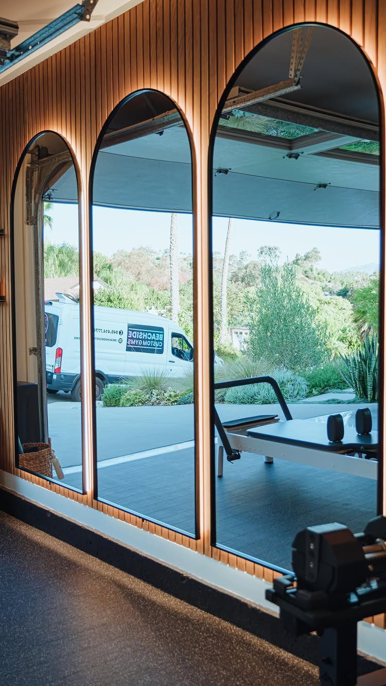 Arched mirrors on a wood wall reflecting a Pilates reformer in a garage gym