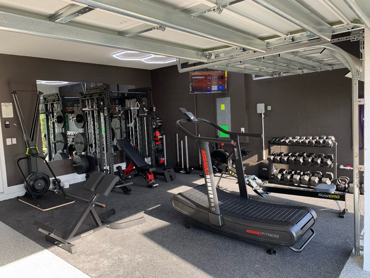 Home garage gym with treadmill, weight bench, and dumbbell rack on rubber flooring
