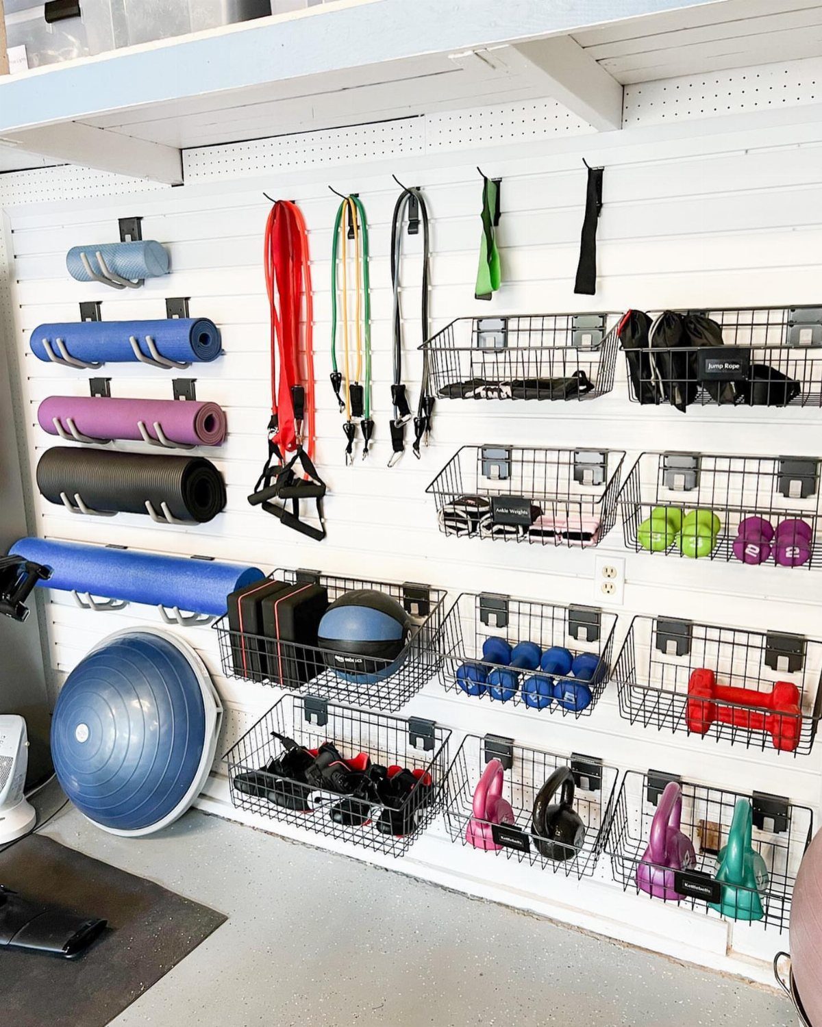 Exercise equipment organized on a white slatwall in a home garage gym.