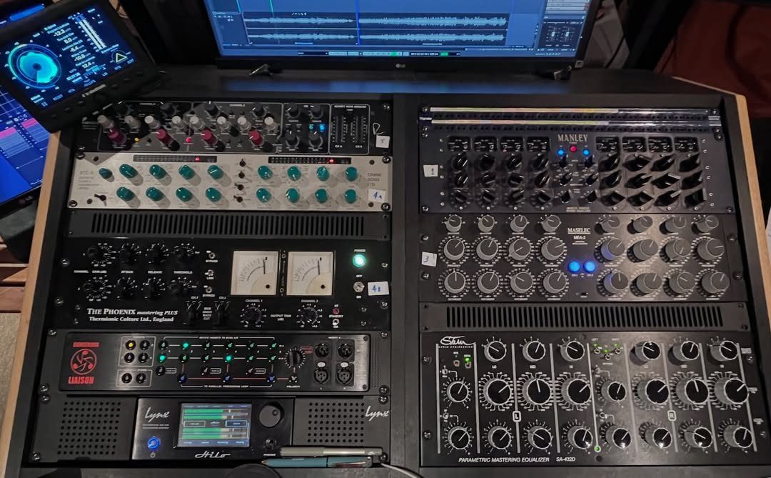 Music studio setup with computer monitor and racks of analog audio processing equipment