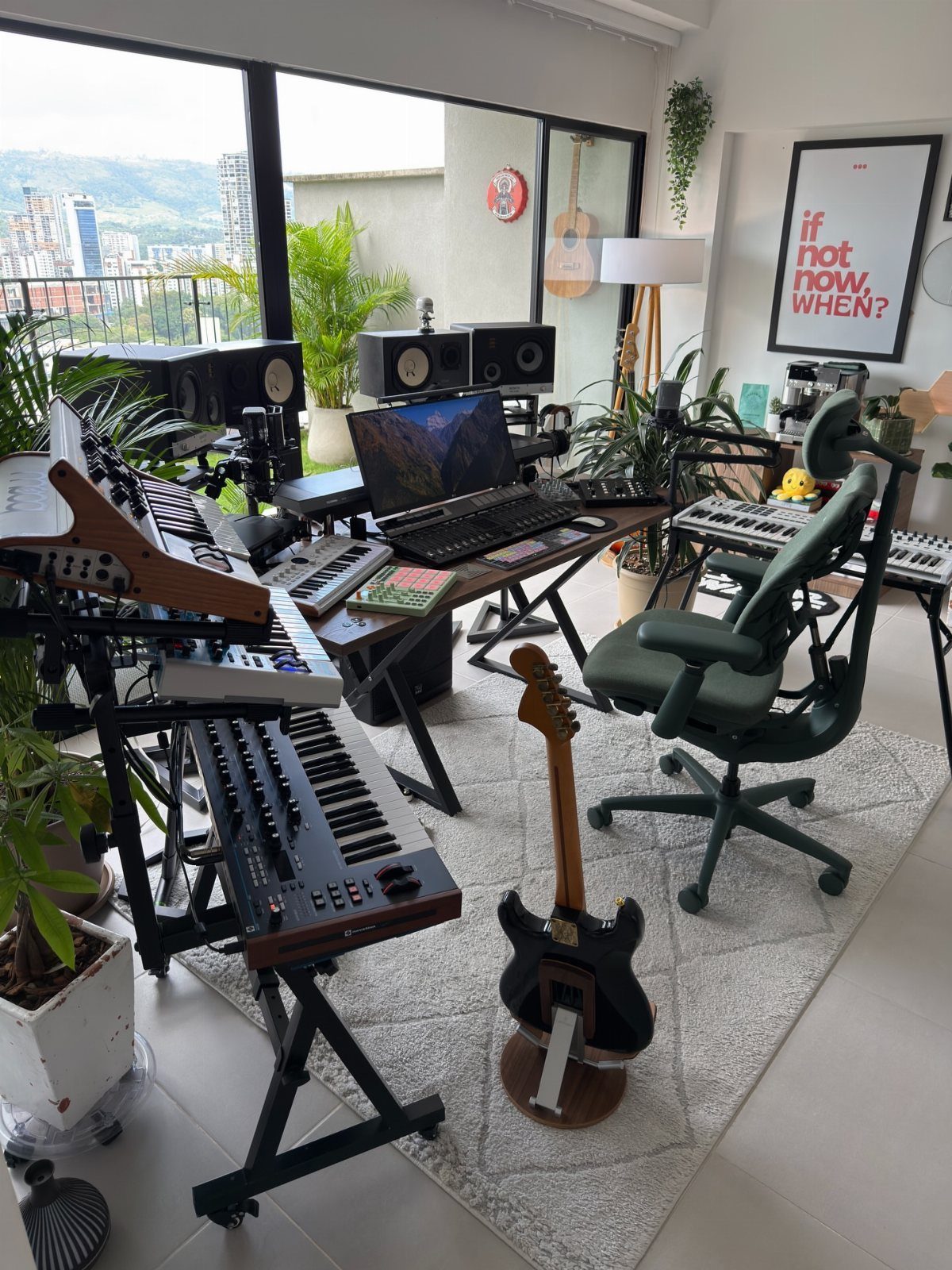 Home music studio with keyboards, electric guitar, and monitors in a bright room.