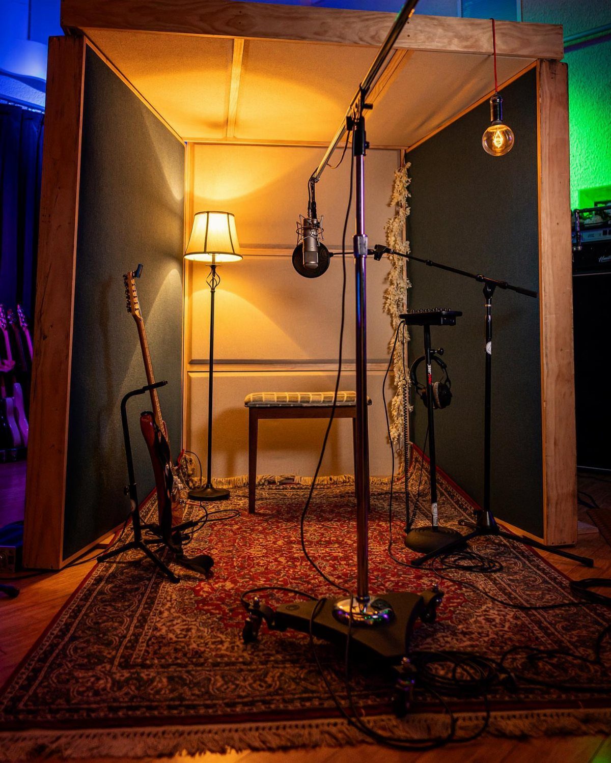 Portable isolation booth with a microphone, electric guitar, and warm lighting on a rug.