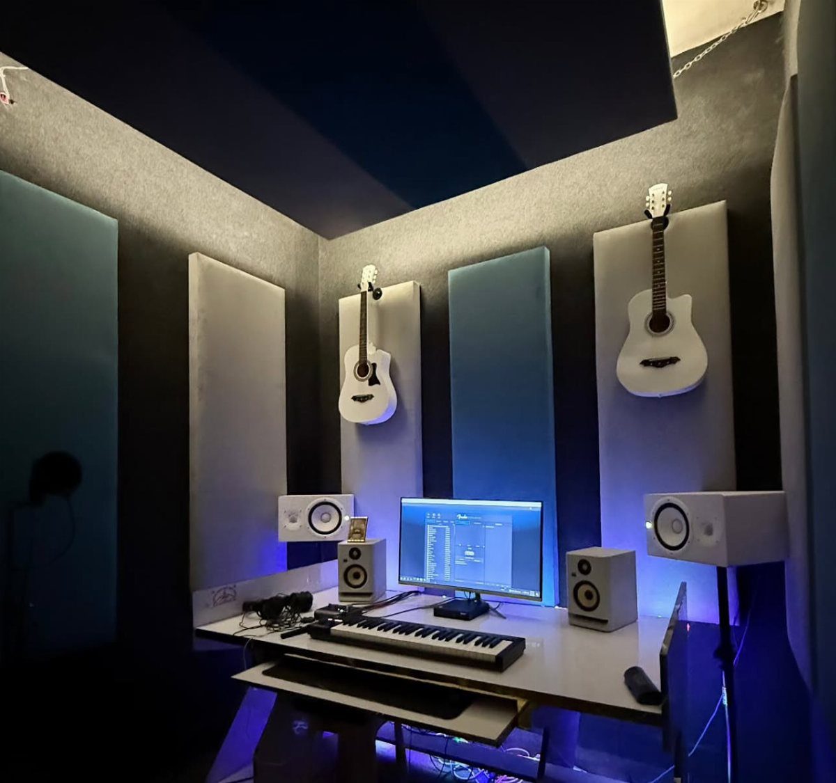 Home music studio with white studio monitors, MIDI keyboard, and acoustic wall panels.