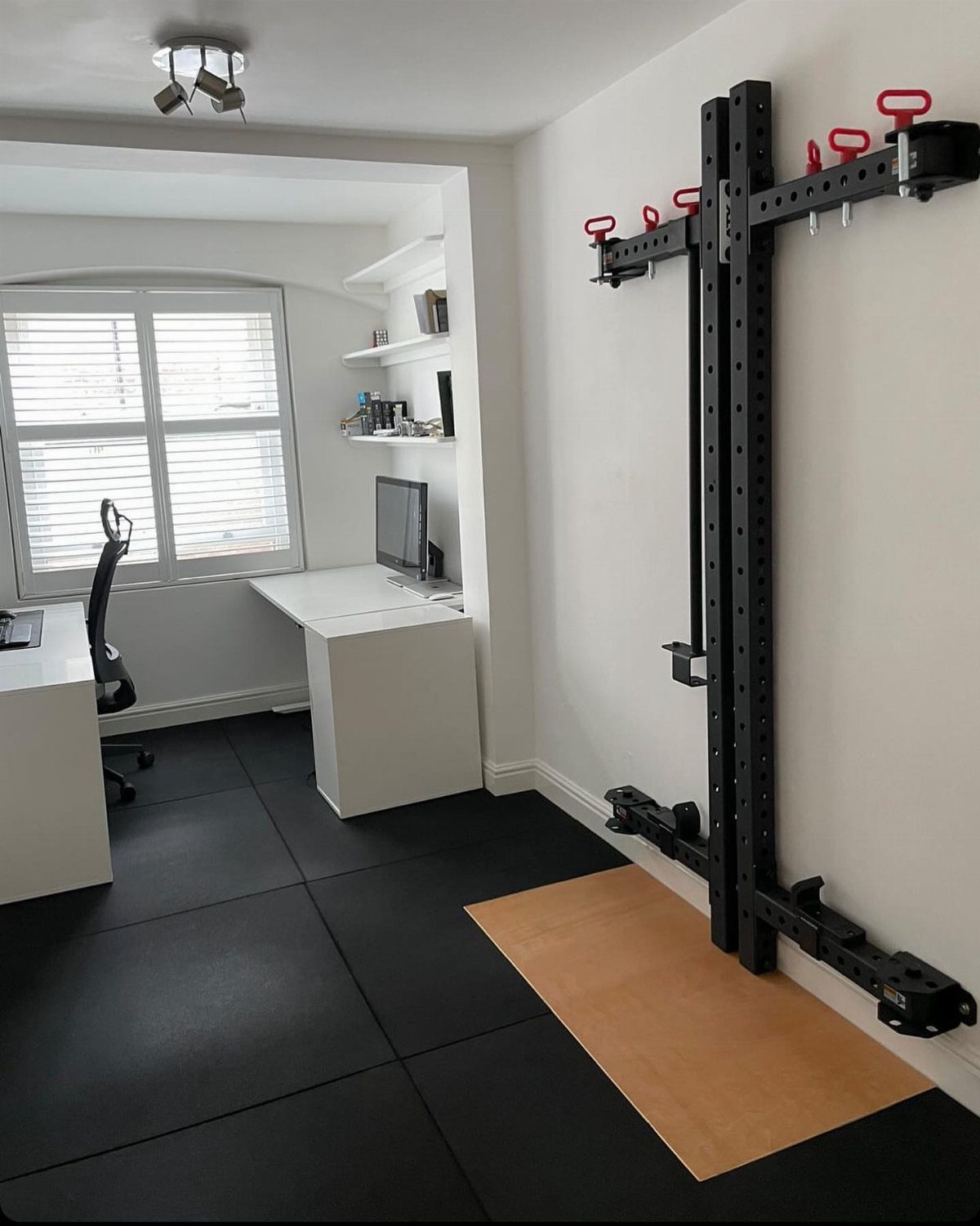 Home office desk and wall-mounted gym rack in a divided multipurpose room.