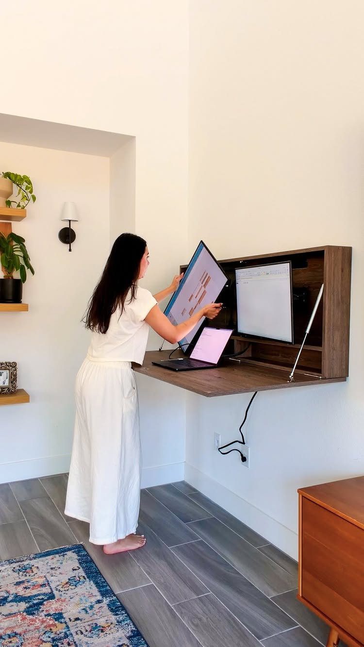 Woman using a brown wooden wall-mounted fold-down desk in a bright white room.