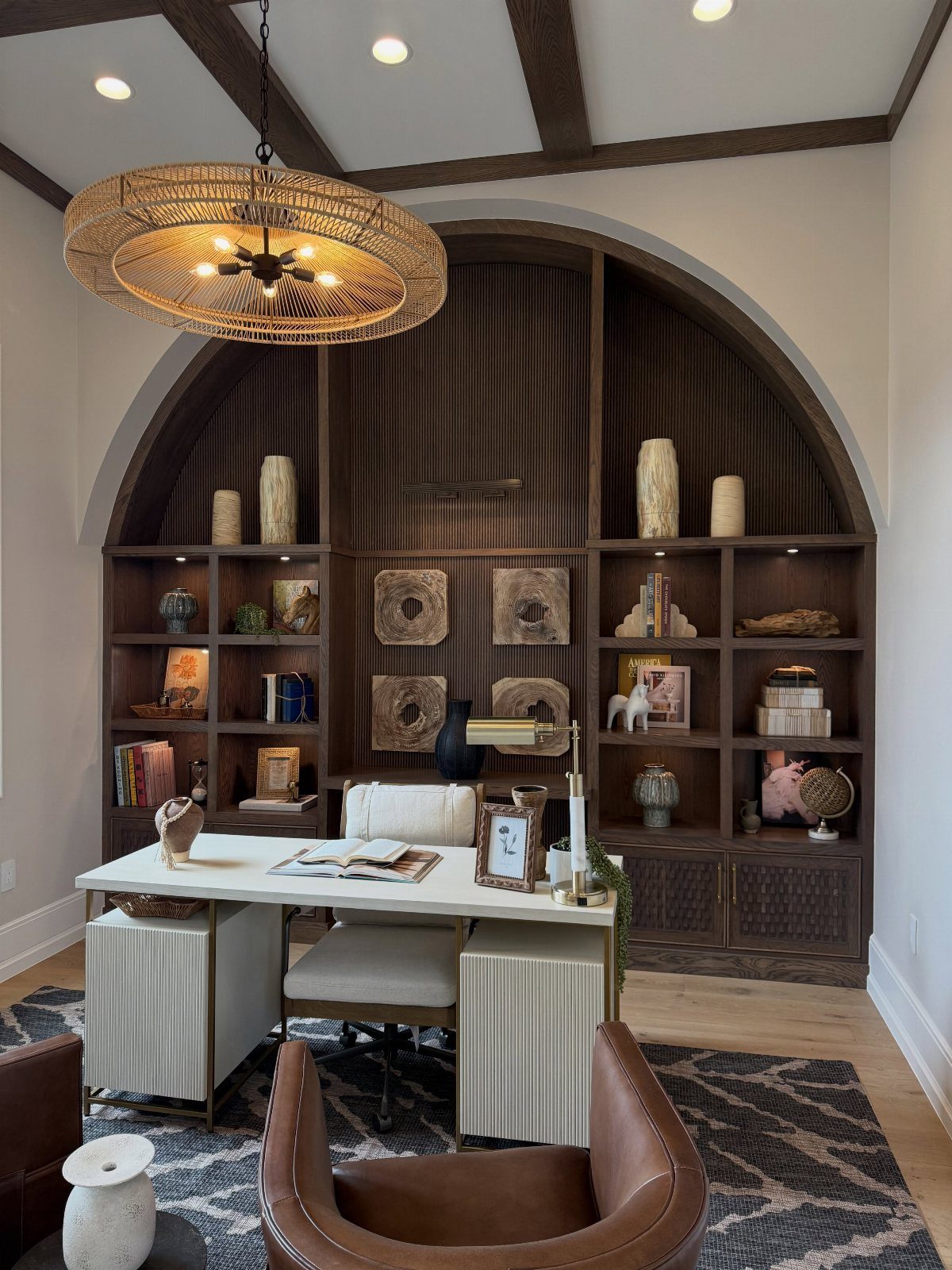 Dark wood arched built-in shelving unit behind a white desk in a home office.
