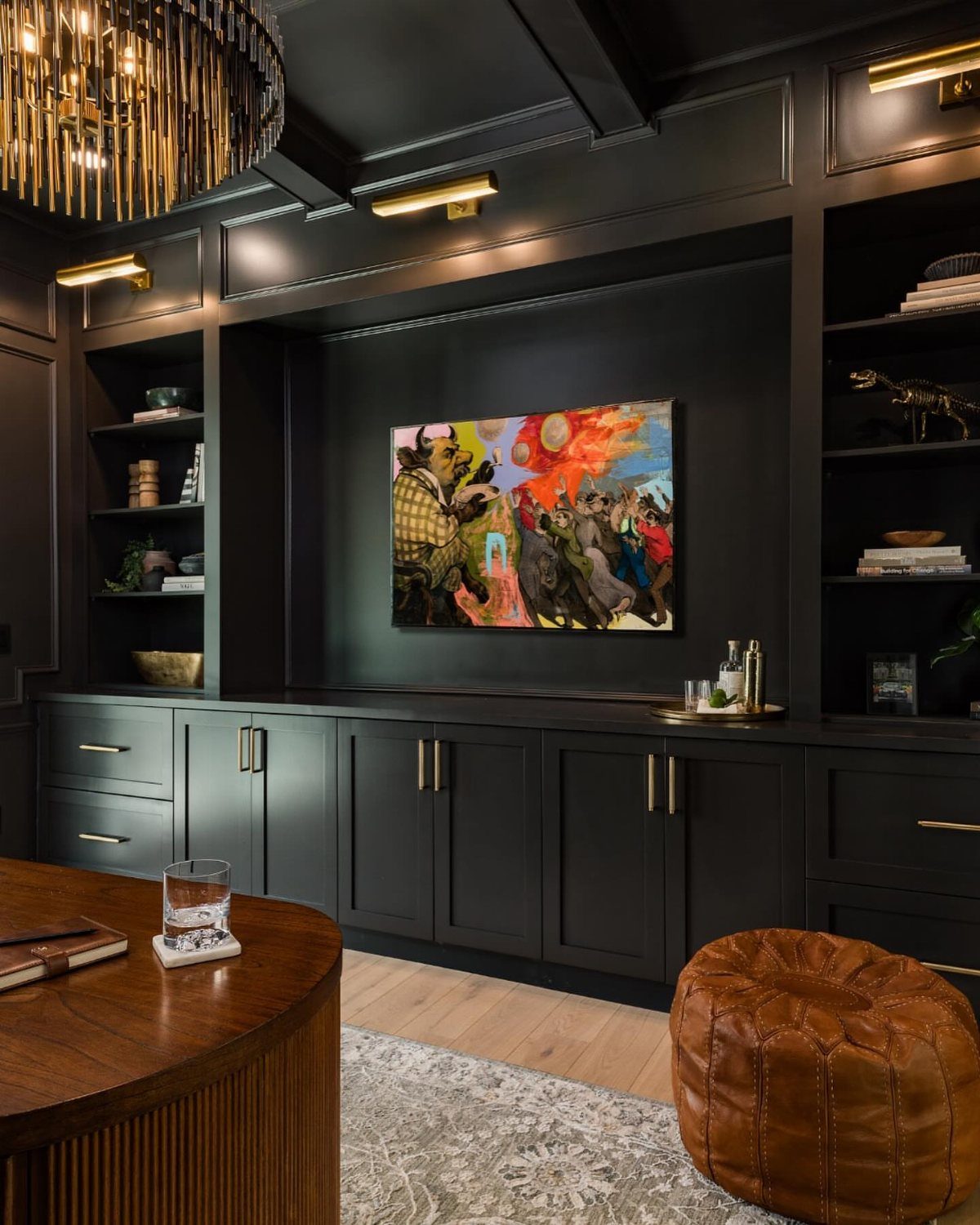 Dark grey built-in office cabinetry with shelving, a central painting, and gold lighting.