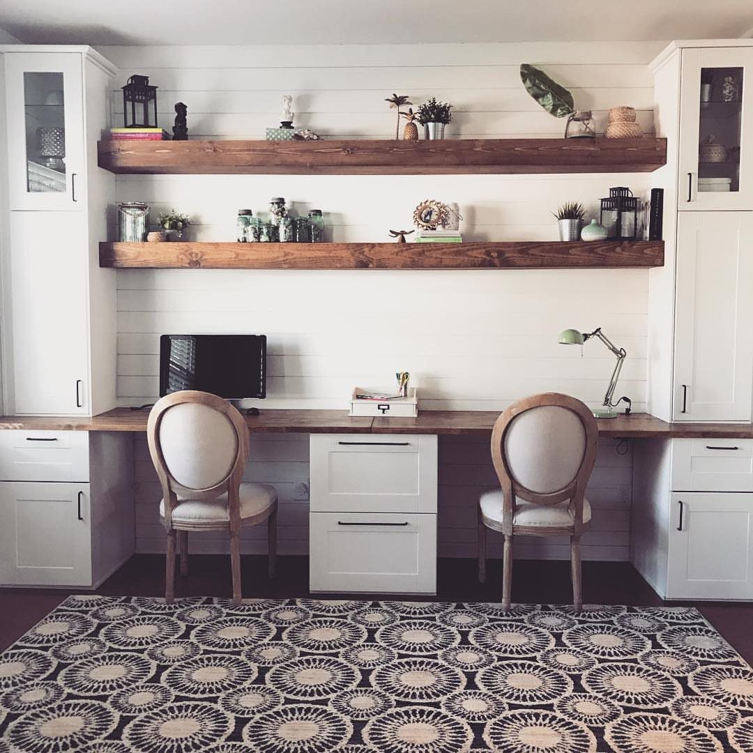 White built-in office cabinets and wooden floating shelves with a long wooden desk.