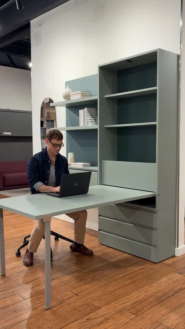 Man working on a laptop at a blue-grey built-in desk and shelving unit.