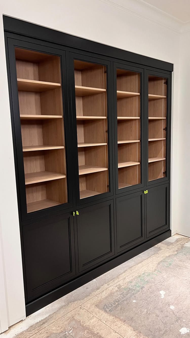 Black built-in shelving unit with glass doors and lower cabinets against white wall
