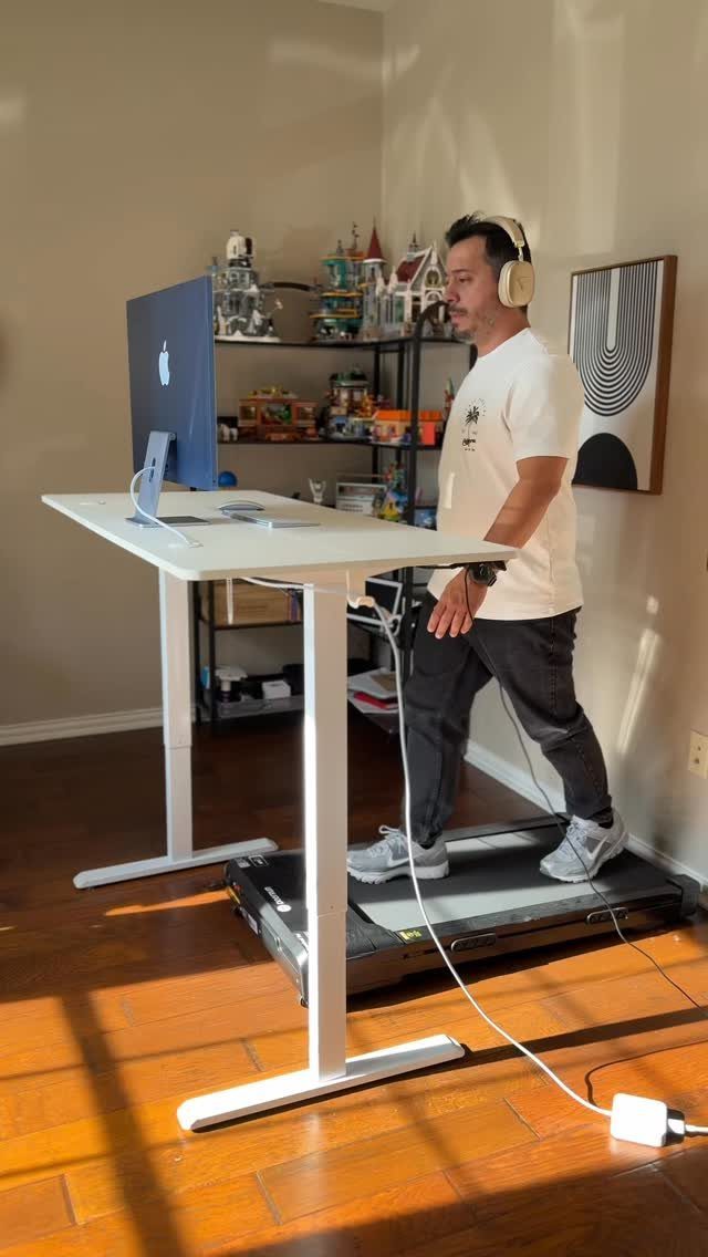 Man using a white adjustable standing desk while walking on a treadmill.