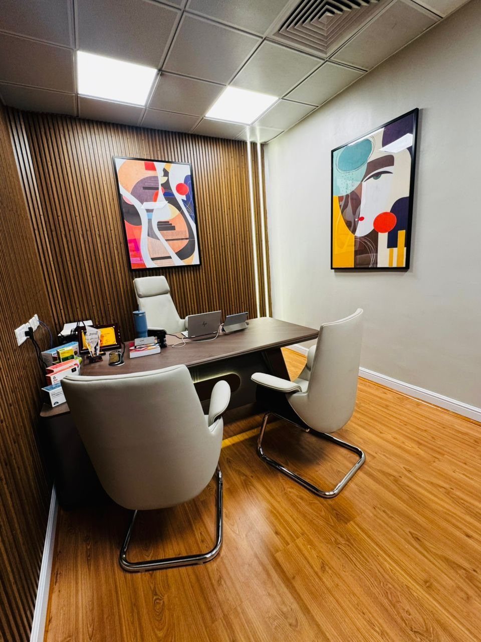 Professional office space with a wooden desk, white chairs, and abstract wall art.