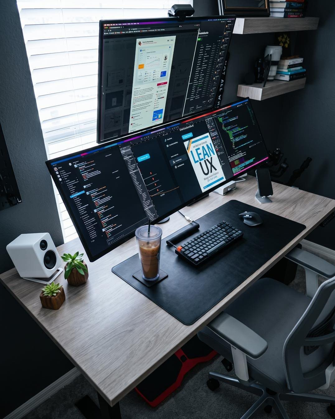 Dual monitors on a light wood desk with a black desk mat and keyboard.