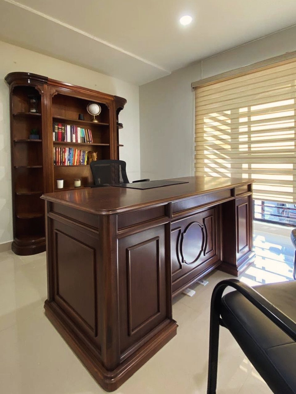 Large dark brown wooden executive desk in a professional home office with bookshelf