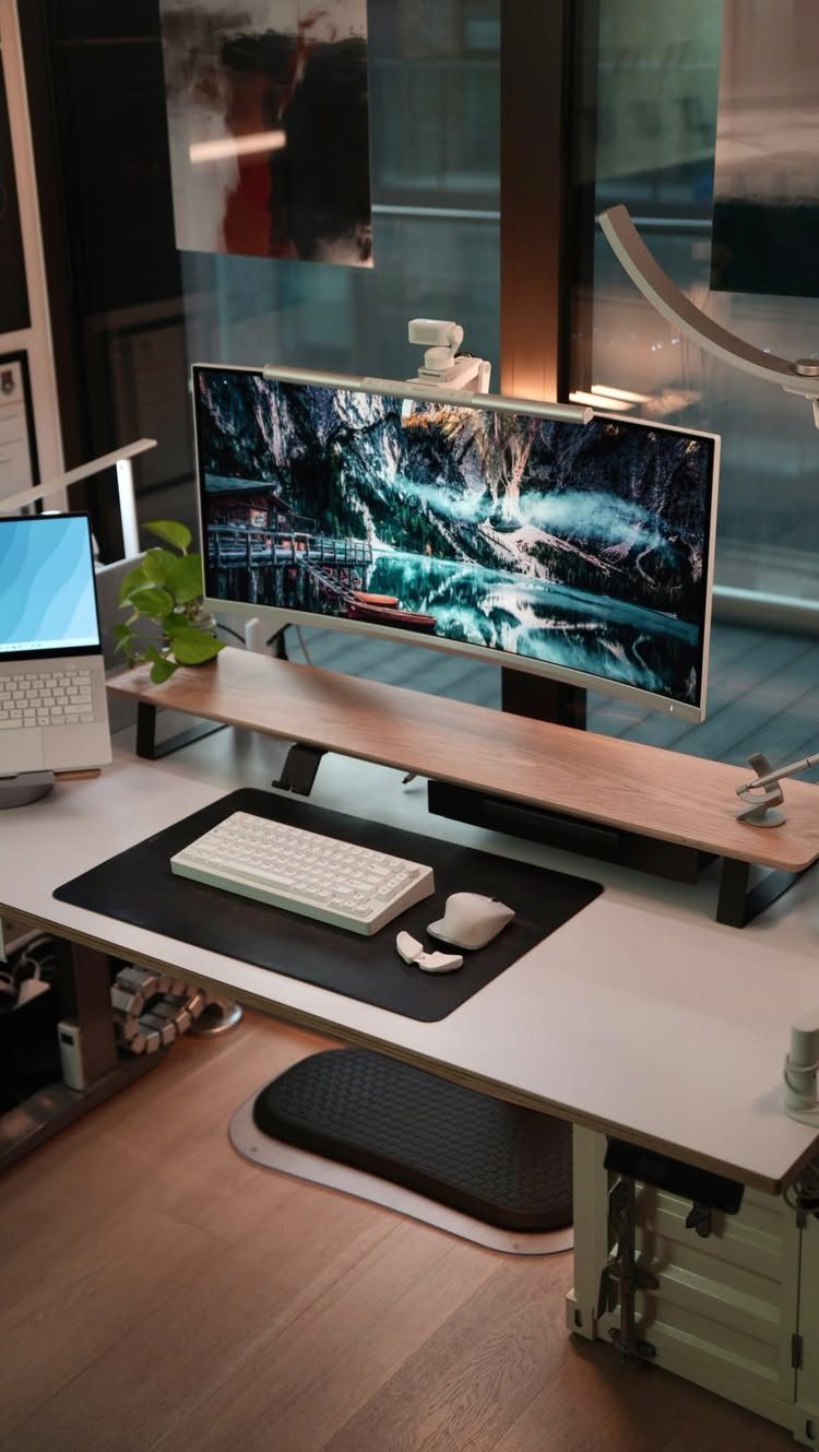 Curved monitor resting on a light wood monitor stand on a white desk.