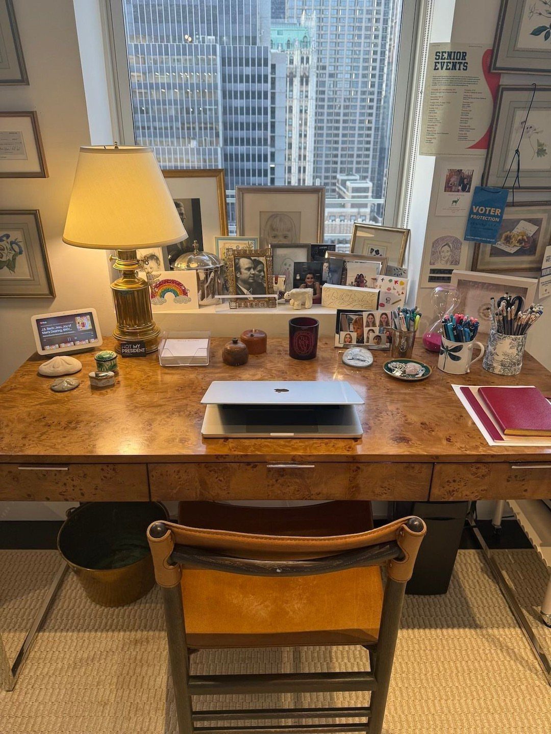 Wooden desk with laptop and personal mementos in front of a city window.