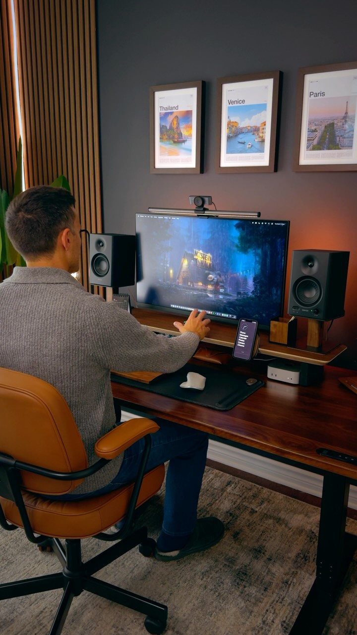 Man working at a wooden desk with a large monitor and studio speakers
