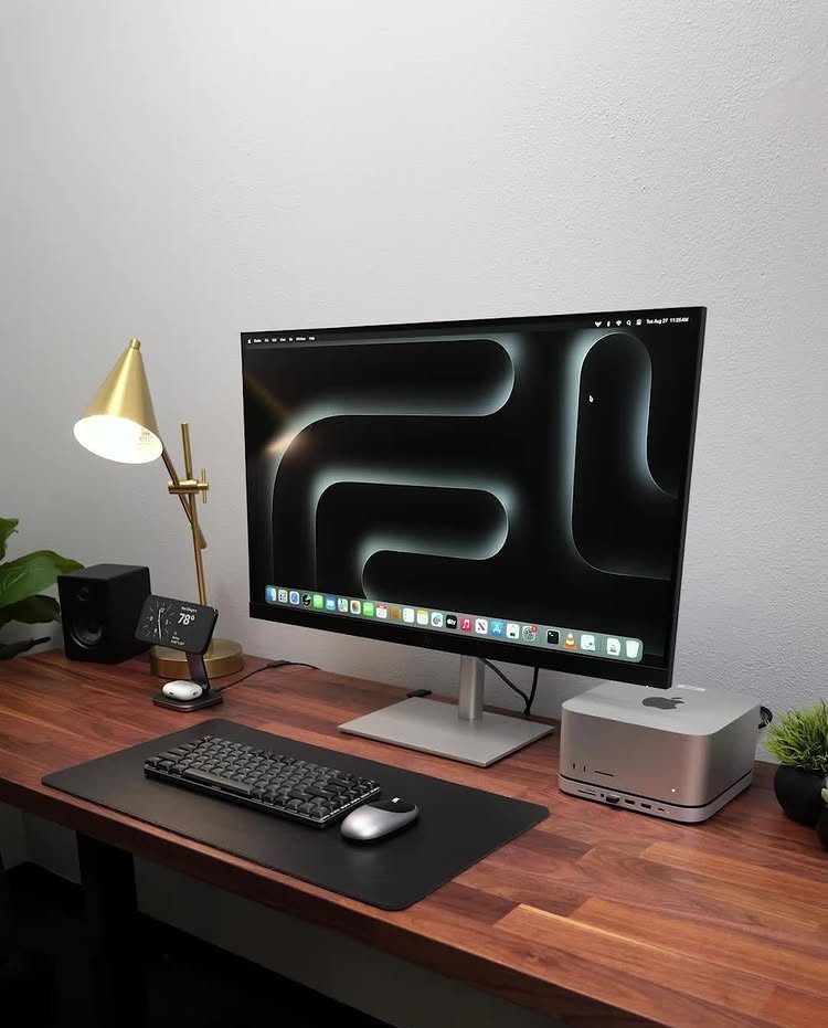 Wooden desk setup with a large monitor, wireless keyboard, mouse, and gold lamp.