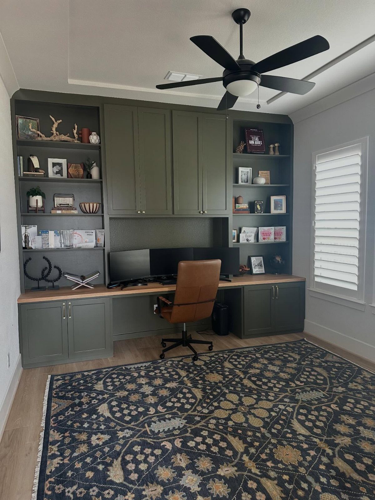 Olive green built-in cabinetry with a wooden desk, leather chair, and patterned rug.