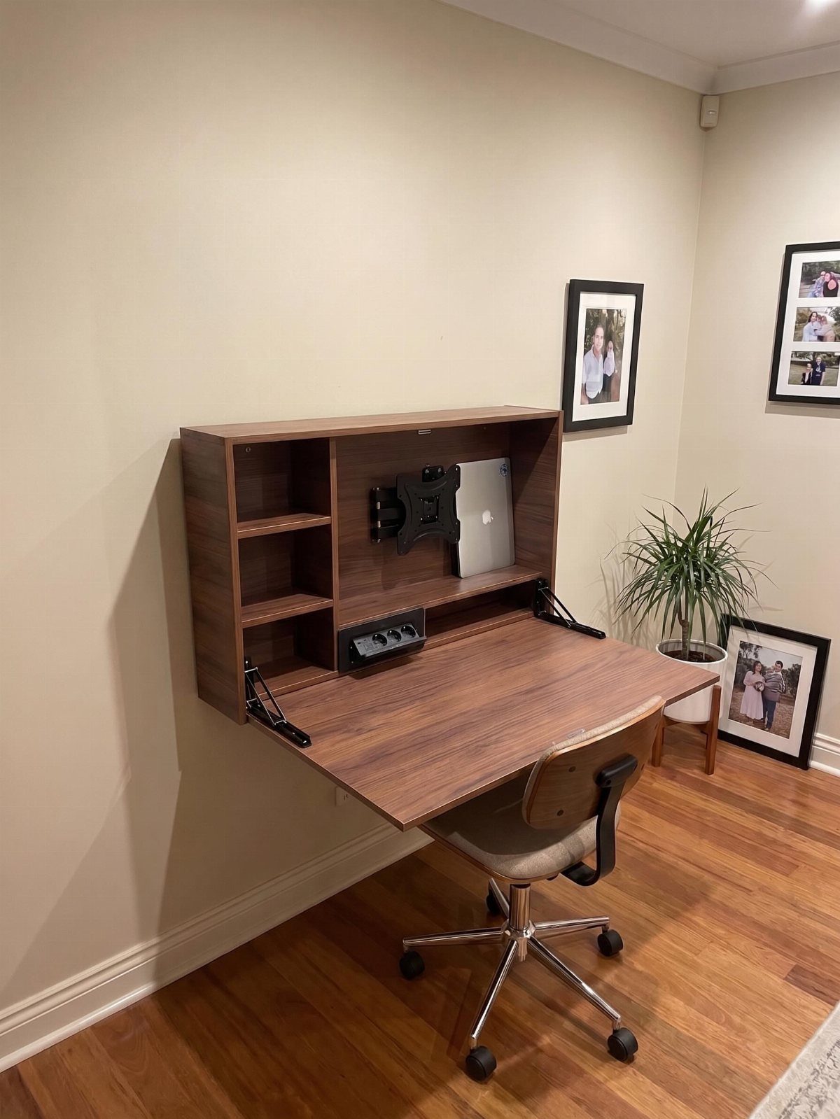 Wall-mounted wooden folding desk with shelving and a beige office chair in a room.